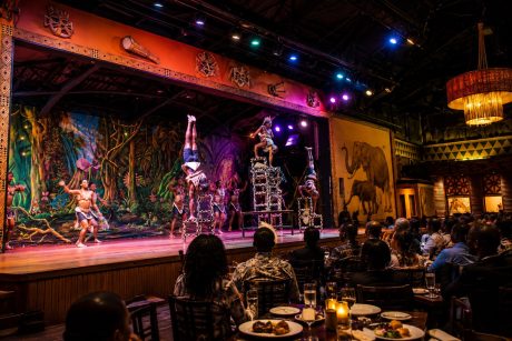Colorful African dancers perform on stage during the Safari Cats Show in Nairobi, with guests enjoying dinner and watching the cultural performance under vibrant theatrical lighting.