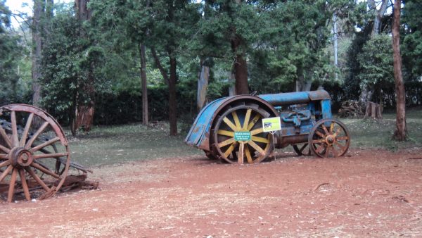 Old tractor and historic farming machinery displayed in the gardens of the Karen Blixen Museum, surrounded by trees