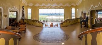 Open-air safari lodge lobby in Masai Mara overlooking vast golden plains with scattered acacia trees and wildlife in the distance.