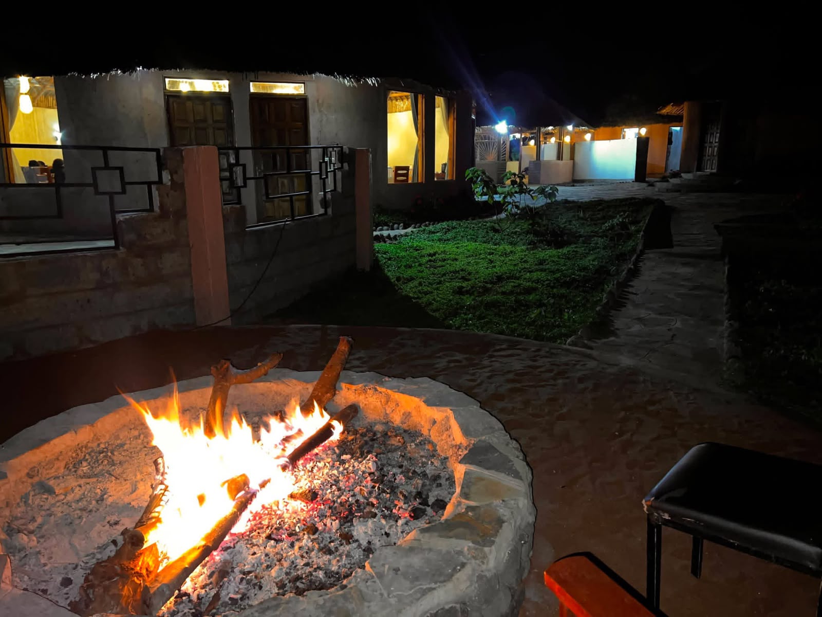 Guests relaxing beside a warm outdoor fireplace at an Amboseli safari lodge in the evening, enjoying the peaceful African atmosphere with Cruzeiro Safaris Kenya.
