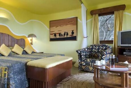 guest room at Mara Serena Safari Lodge featuring a king-size bed, African-inspired décor, lounge seating, and modern amenities in the Maasai Mara, Kenya.